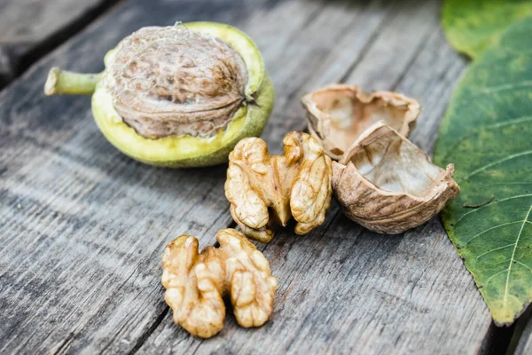 Nueces frescas en una cáscara verde cerca del núcleo de la nuez en una mesa de madera vieja. Nueces en conchas verdes . —  Fotos de Stock