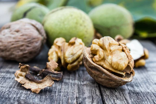 Καρύδια καρύδια και ολόκληρα καρύδια βρίσκονται δίπλα σε ξηρούς καρπούς με πράσινα κοχύλια και πράσινα φύλλα σε ένα ρουστίκ παλιό ξύλινο τραπέζι. — Φωτογραφία Αρχείου