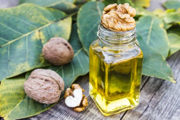 Walnut oil in a glass jar near walnuts and green leaves on a wooden table. — Stockfoto