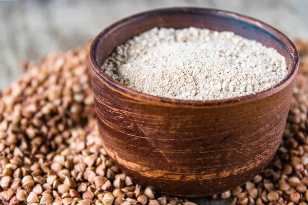 Buckwheat flour in a bowl near the buckwheat grain. A pile of buckwheat flour.