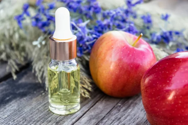 Стеклянная бутылка яблочного эфирного масла возле свежих яблок на деревянном столе. Эфирное масло используется для наполнения светильников, парфюмерии и косметики . — стоковое фото