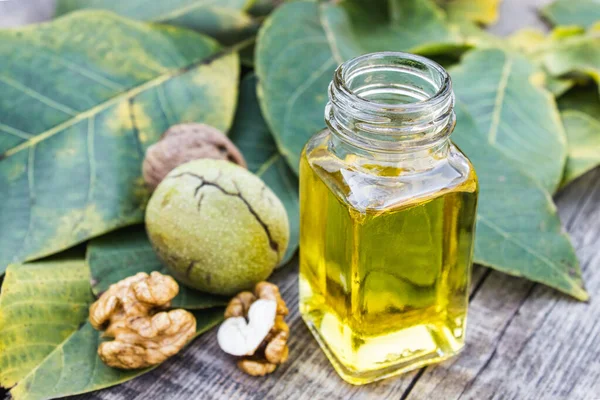 Walnut oil in a glass jar near walnuts and green leaves on a wooden table. — Stockfoto