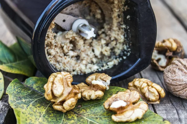 Нарезанный грецкий орех в кофемолке возле орехового ядра на старом деревянном столе . — стоковое фото