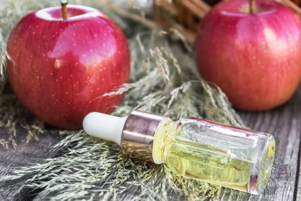 Minyak esensial Apple di meja kayu dekat apel merah matang. Minyak esensial digunakan untuk mengisi lampu, parfum, dan kosmetik . — Stok Foto