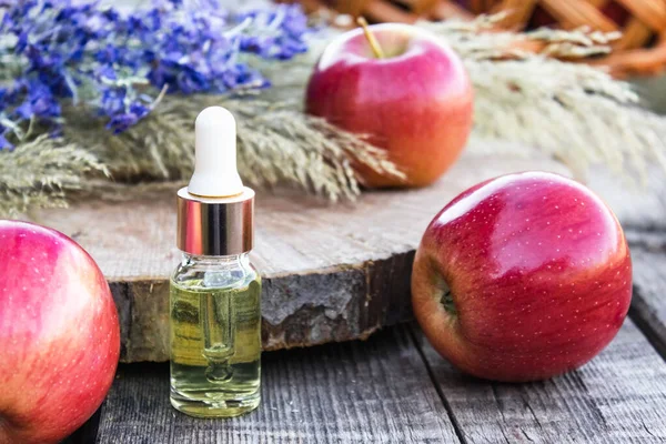Botol kaca minyak esensial apel dekat apel segar di atas meja kayu. Minyak esensial digunakan untuk mengisi lampu, parfum, dan kosmetik . — Stok Foto
