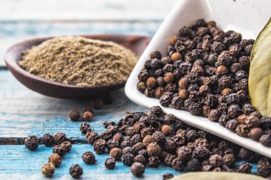 Masaya saçılmış bezelyelerin yanında bir kaşık içinde kara biber ve mavi tahtaların arka planında bir defne yaprağı bulunur. Pişirmek için karabiber ve baharat.