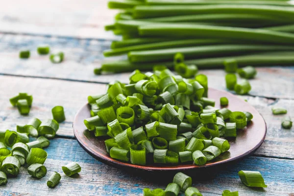 Taze yeşil soğan dilimlenmiş ve mavi panoların arka planında bir kasenin üzerinde yatıyor. Frenk soğanlarının birçok vitamini ve minerali vardır..