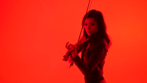 苗条性感的年轻亚洲女孩在紧身黑色皮革衣服表现在红色背景上弹奏电动小提琴 — 图库视频影像