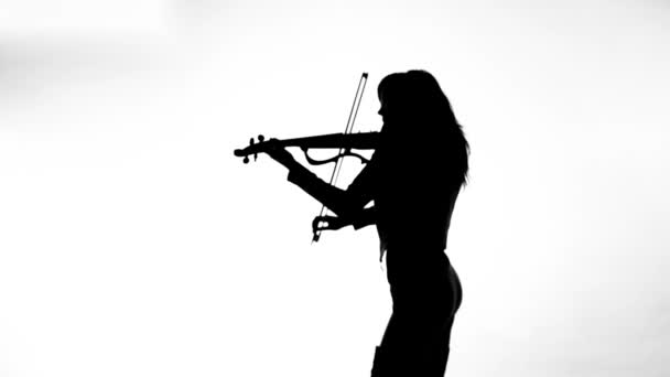 タイトな黒い革の服を着た白い背景の若い女の子に黒いシルエットは 表現力豊かに電気バイオリンを果たしています — ストック動画