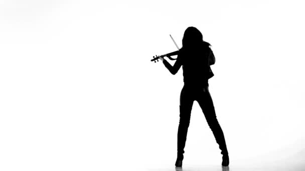 タイトな黒い革の服を着た白い背景の若い女の子に黒いシルエットは 表現力豊かに電気バイオリンを果たしています — ストック動画