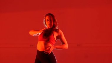 Genç ve güzel bir kadın kırmızı arka planda dans ediyor.