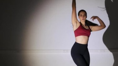 Genç ve güzel bir kadın yüksek topuklularla modern dans ediyor, striptiz dansı, moda, gölge hareketlerini tekrarlıyor.