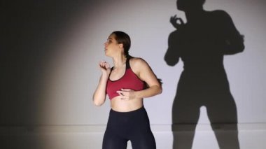 Genç ve güzel bir kadın yüksek topuklularla modern dans ediyor, striptiz dansı, moda, gölge hareketlerini tekrarlıyor.