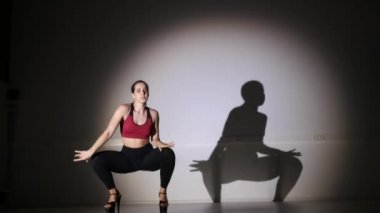 Genç ve güzel bir kadın yüksek topuklularla modern dans ediyor, striptiz dansı, moda, gölge hareketlerini tekrarlıyor.