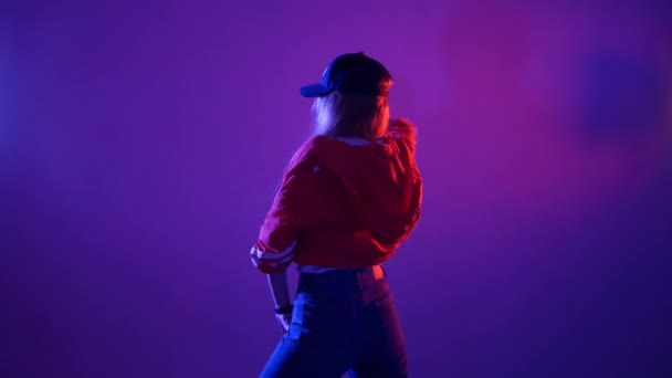 野球帽をかぶった若い美女がヒップホップを踊りスタジオで紫の背景でストリートダンスをし孤立した — ストック動画
