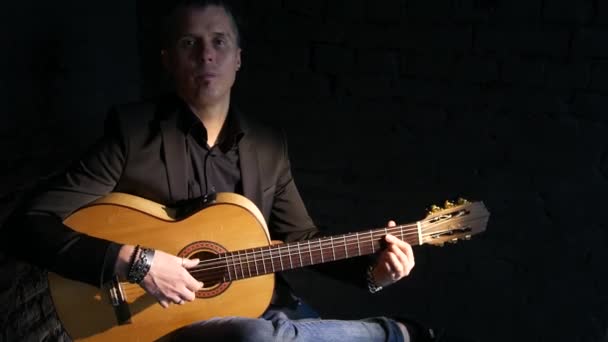 黒レンガの壁の背景にフラメンコ音楽を演奏ギタープレーヤー — ストック動画