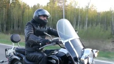 Kasklı erkek bisikletçi gün batımında orman yolu boyunca motosikletsürüyor