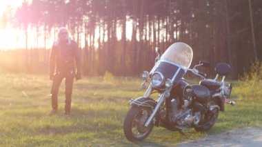 uzun gri saçlı yetişkin adam gün batımında ormanda bir motosiklet üzerinde oturur