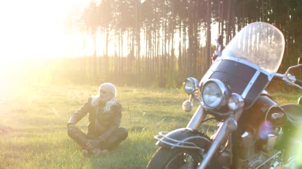 成年男子长灰色的头发坐在草地上附近的摩托车在日落 — 图库视频影像