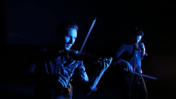 二重奏的年轻音乐家演奏电动大提琴和电动小提琴在黑色背景 — 图库视频影像