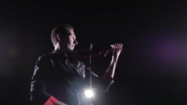 Genç yakışıklı adam siyah arka planda elektrikli keman çalıyor.
