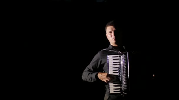 若い音楽家のヴィルトゥオーゾは黒を背景にスタジオでアコーディオンを演奏します — ストック動画