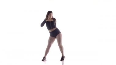 Uzun saçlı, uzun saçlı, genç, şehvetli bir dansçı kız. Tayt ve şortla dans ediyor. Dans pisti twerk dansı, modern dans, kalçalarını sallıyor.