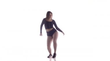 Uzun saçlı, uzun saçlı, genç, şehvetli bir dansçı kız. Tayt ve şortla dans ediyor. Dans pisti twerk dansı, modern dans, kalçalarını sallıyor.