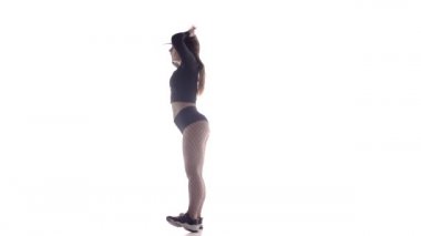 Uzun saçlı, uzun saçlı, genç, şehvetli bir dansçı kız. Tayt ve şortla dans ediyor. Dans pisti twerk dansı, modern dans, kalçalarını sallıyor.