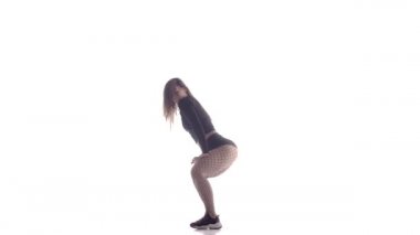 Uzun saçlı, uzun saçlı, genç, şehvetli bir dansçı kız. Tayt ve şortla dans ediyor. Dans pisti twerk dansı, modern dans, kalçalarını sallıyor.