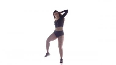 Uzun saçlı, uzun saçlı, genç, şehvetli bir dansçı kız. Tayt ve şortla dans ediyor. Dans pisti twerk dansı, modern dans, kalçalarını sallıyor.