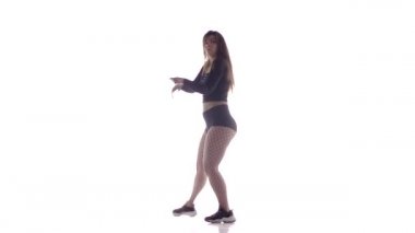Uzun saçlı, uzun saçlı, genç, şehvetli bir dansçı kız. Tayt ve şortla dans ediyor. Dans pisti twerk dansı, modern dans, kalçalarını sallıyor.
