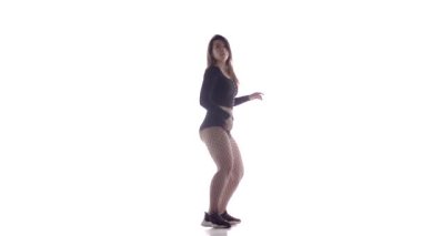 Uzun saçlı, uzun saçlı, genç, şehvetli bir dansçı kız. Tayt ve şortla dans ediyor. Dans pisti twerk dansı, modern dans, kalçalarını sallıyor.