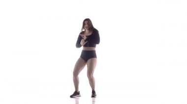 Uzun saçlı, uzun saçlı, genç, şehvetli bir dansçı kız. Tayt ve şortla dans ediyor. Dans pisti twerk dansı, modern dans, kalçalarını sallıyor.