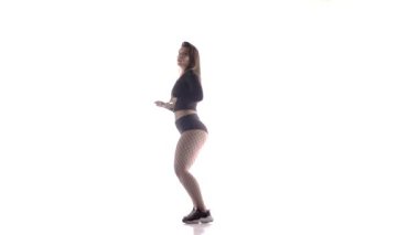 Uzun saçlı, uzun saçlı, genç, şehvetli bir dansçı kız. Tayt ve şortla dans ediyor. Dans pisti twerk dansı, modern dans, kalçalarını sallıyor.