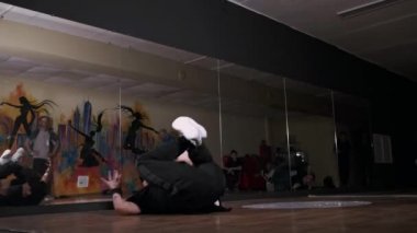 Genç çocuk modern dans gösterisi yapıyor, yeldeğirmeni yapıyor ve yavaş çekimde aynalarla jimnastik salonunda dans ediyor. Diğer dansçılar yakınlarda duruyor. Dans okulu. Gençlik alt kültürü.