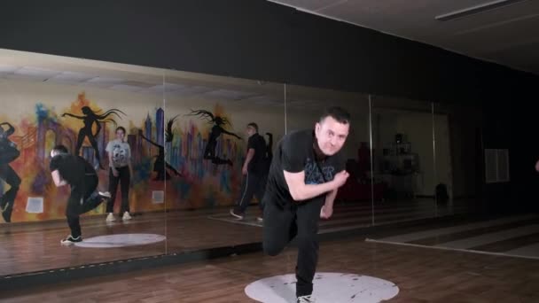 一个活跃的年轻人跳嘻哈舞的视频 附近站着其他舞者 舞蹈学校 改进霹雳舞技巧的概念 青年亚文化 当代编舞 慢动作 — 图库视频影像