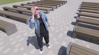 Genç adam banklar arasında parkta sokak dansı yapıyor. Hip hop ve break dans tekniği öğrenme kavramı. Gençlik alt kültürü. Çağdaş koreografi. Yavaş çekim