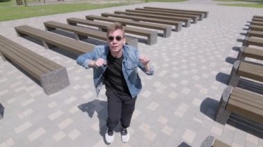 Genç adam banklar arasında parkta sokak dansı yapıyor. Hip hop ve break dans tekniği öğrenme kavramı. Gençlik alt kültürü. Çağdaş koreografi. Yavaş çekim
