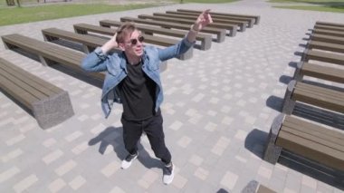 Genç adam banklar arasında parkta sokak dansı yapıyor. Hip hop ve break dans tekniği öğrenme kavramı. Gençlik alt kültürü. Çağdaş koreografi. Yavaş çekim