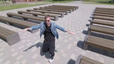 Genç adam banklar arasında parkta sokak dansı yapıyor. Hip hop ve break dans tekniği öğrenme kavramı. Gençlik alt kültürü. Çağdaş koreografi. Yavaş çekim