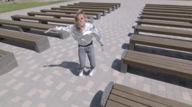 Genç kız dans edip modern koreografi ya da halk parkında şehirdeki banklar arasında sokak dansı yapıyor. Gençlik alt kültürü. Çağdaş koreografi. Ağır çekim. Düşük çekim noktası