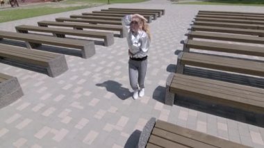 Genç kız dans edip modern koreografi ya da halk parkında şehirdeki banklar arasında sokak dansı yapıyor. Gençlik alt kültürü. Çağdaş koreografi. Ağır çekim. Düşük çekim noktası