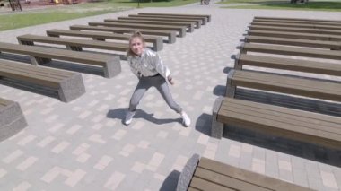 Genç kız dans edip modern koreografi ya da halk parkında şehirdeki banklar arasında sokak dansı yapıyor. Gençlik alt kültürü. Çağdaş koreografi. Ağır çekim. Düşük çekim noktası