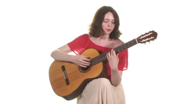年轻美丽的女人 身穿红色衬衫 头戴大括号 用古典的声学吉他演唱和伴奏 中远距离射击 被隔离了 — 图库视频影像