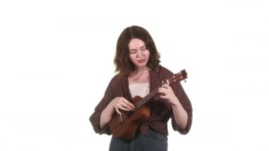 Ekose gömlekli genç bir müzisyen kız sahne ışıkları önünde ukulele çalıyor. İzole edilmiş. Orta uzunlukta.