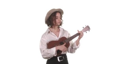 Beyaz bluzlu ve şapkalı güzel kız ukulele çalıyor. İzole edilmiş. Orta uzunlukta.