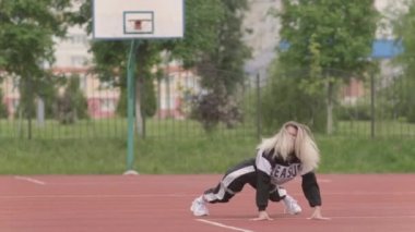 Eşofmanlı, uzun saçlı enerjik genç bir kadın sokak dansı, dans pisti twerk, kalçalarını bir spor sahasında sallıyor. Şehirde şehir dansı serbest stil