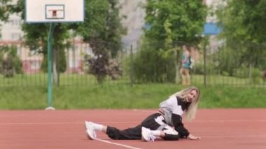Eşofmanlı, uzun saçlı enerjik genç bir kadın sokak dansı, dans pisti twerk, kalçalarını bir spor sahasında sallıyor. Şehirde şehir dansı serbest stil