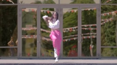 Yetenekli kız binanın önünde dans ediyor. Hiphop ve break dans tekniklerini öğrenme kavramı. Gençlik alt kültürü. Çağdaş koreografi. Yavaş çekim